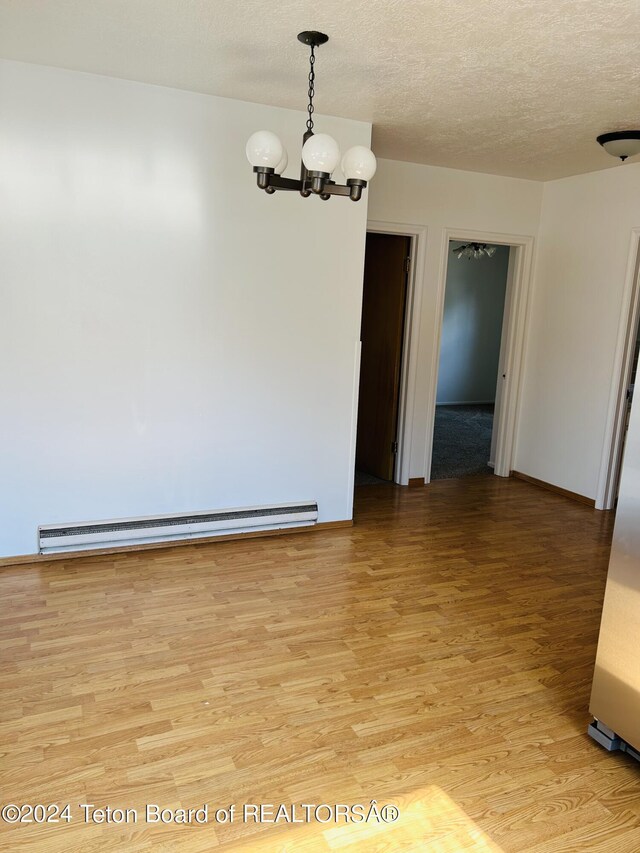 spare room featuring a notable chandelier, light hardwood / wood-style flooring, baseboard heating, and a textured ceiling