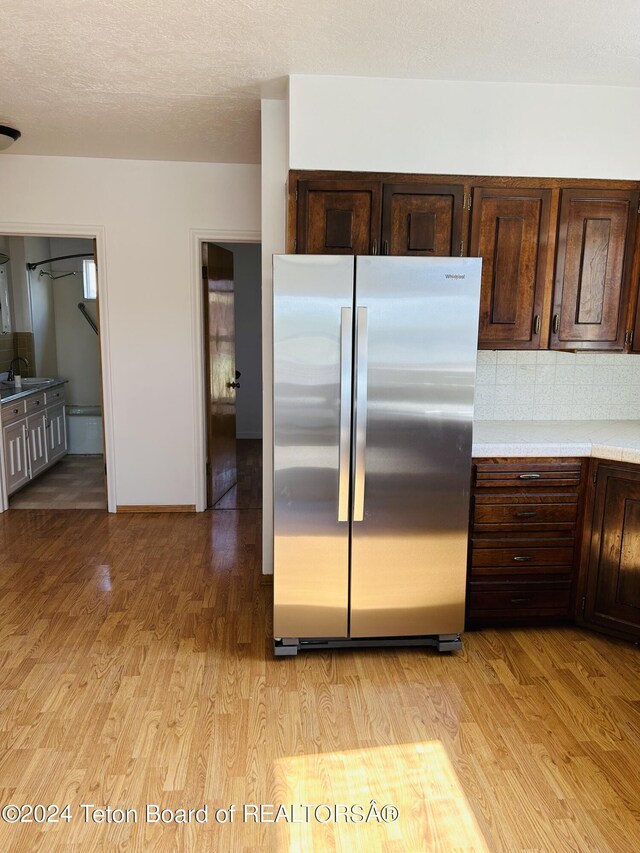 kitchen with backsplash, light hardwood / wood-style floors, stainless steel refrigerator, and sink