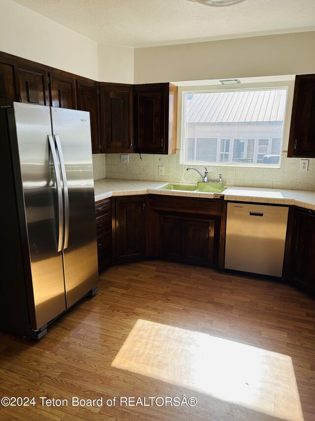 kitchen with tasteful backsplash, stainless steel appliances, sink, dark brown cabinetry, and light hardwood / wood-style flooring