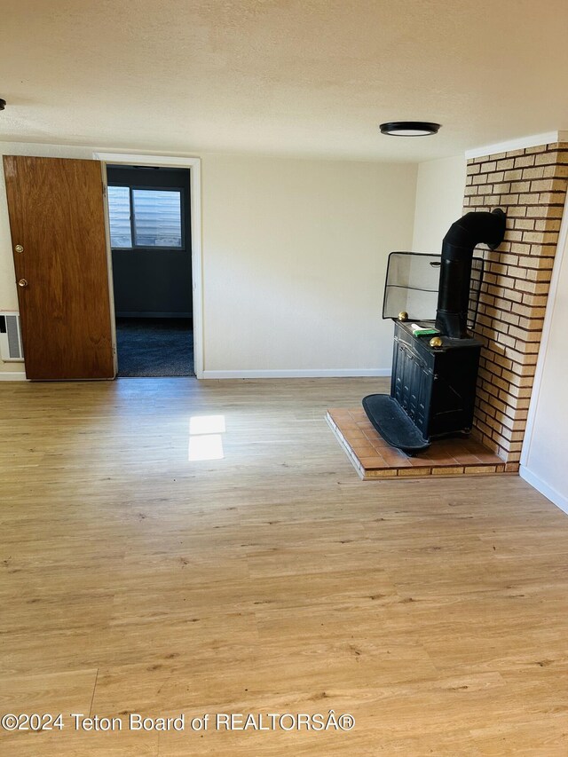 unfurnished living room with a wood stove, light hardwood / wood-style floors, brick wall, and a textured ceiling