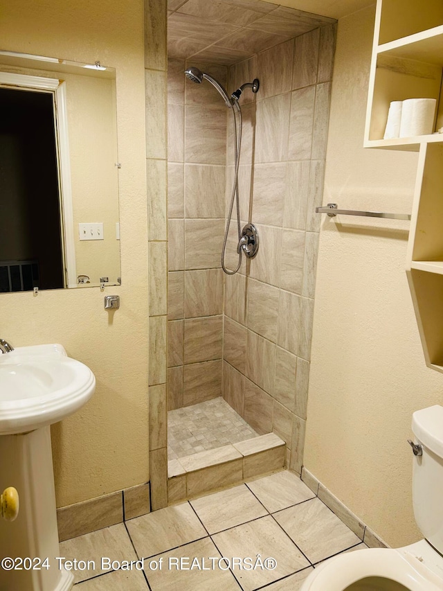 bathroom with tiled shower, toilet, and tile patterned flooring