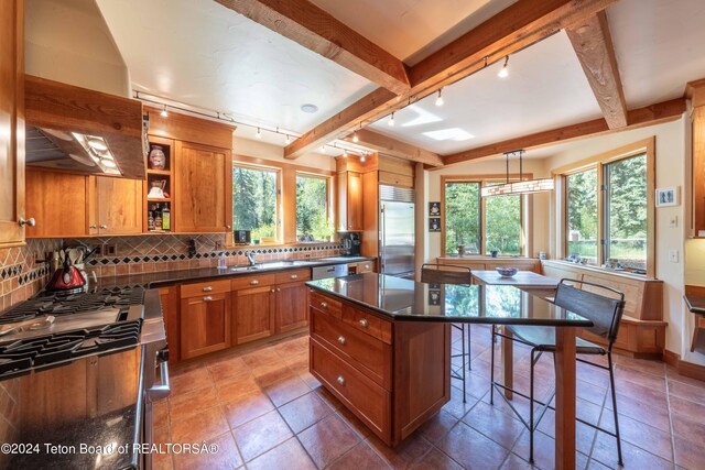 155 E Buck Mountain Rd, Jackson, WY 83001 - kitchen with decorative backsplash, brown cabinets, dark countertops, beam ceiling, and appliances with stainless steel finishes