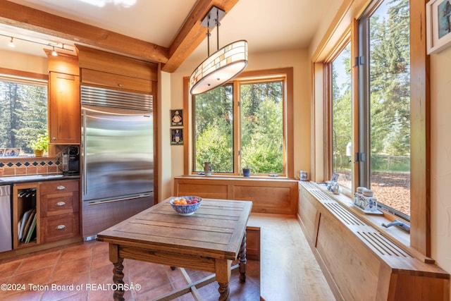 interior space featuring backsplash, rail lighting, built in refrigerator, light tile patterned floors, and hanging light fixtures