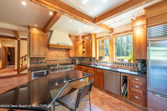 kitchen with beamed ceiling, premium range hood, built in appliances, and tasteful backsplash