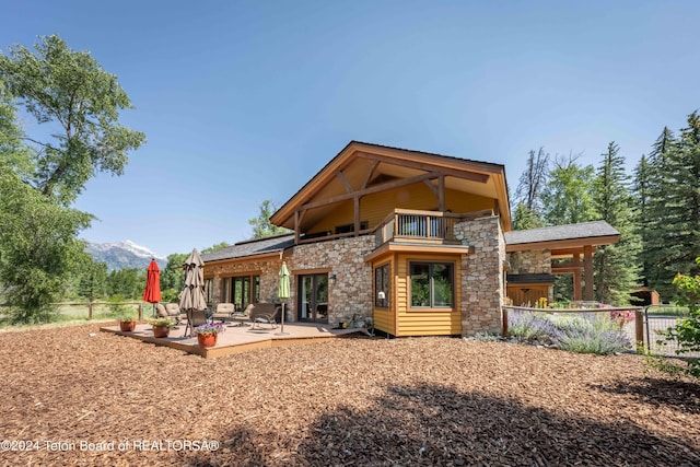 155 E Buck Mountain Rd, Jackson, WY 83001 - rear view of house featuring stone siding, a balcony, a mountain view, and fence