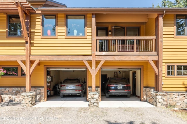 155 E Buck Mountain Rd, Jackson, WY 83001 - view of front of home with stone siding, an attached garage, a balcony, and driveway