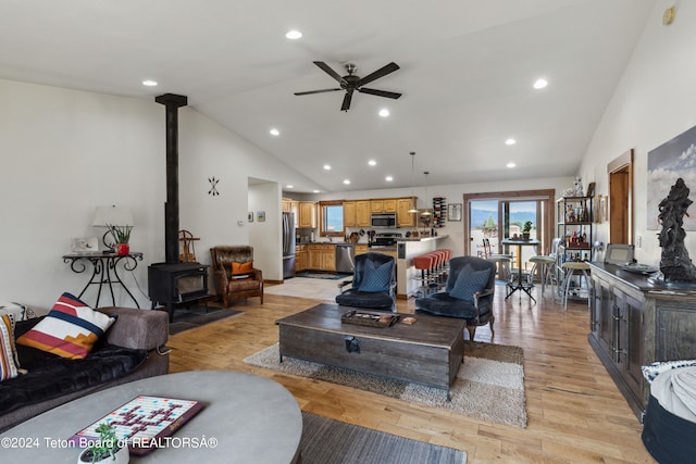 living room with ceiling fan, light hardwood / wood-style flooring, high vaulted ceiling, and a wood stove