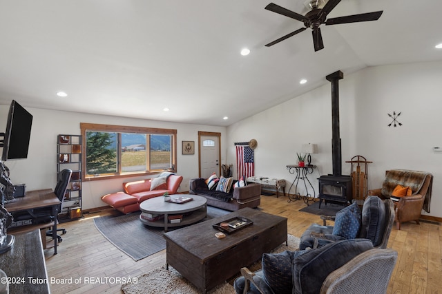 living room with light wood-type flooring, ceiling fan, lofted ceiling, and a wood stove