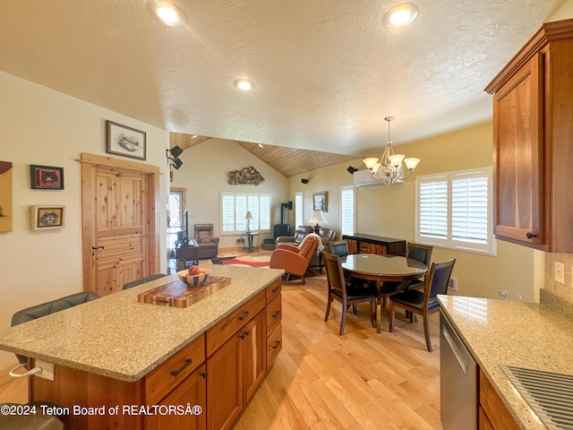 kitchen featuring vaulted ceiling, hanging light fixtures, light hardwood / wood-style flooring, stainless steel dishwasher, and light stone countertops