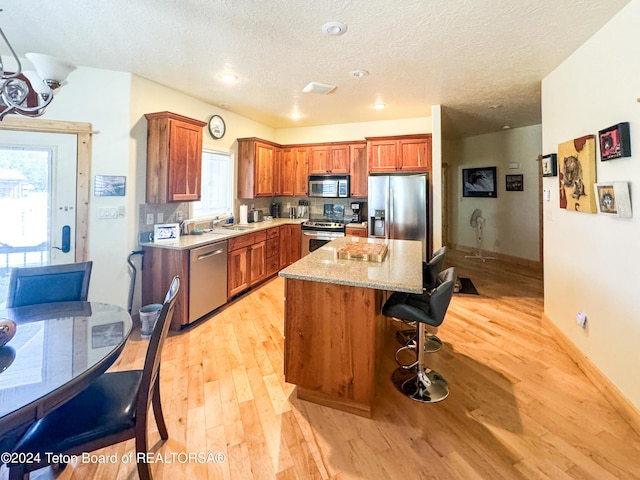 kitchen with sink, light wood-type flooring, a kitchen island, stainless steel appliances, and light stone countertops