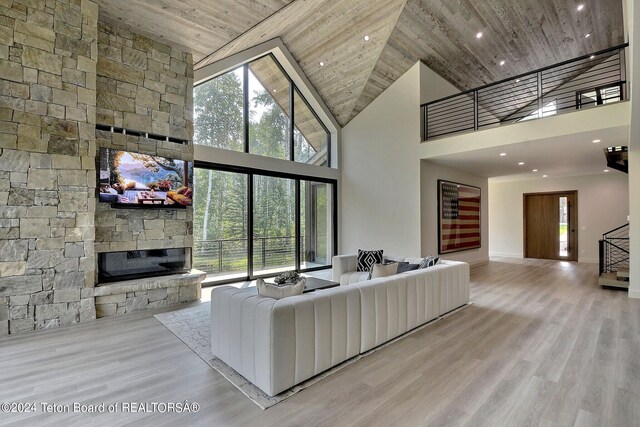 unfurnished living room with high vaulted ceiling, light wood-type flooring, a stone fireplace, and wooden ceiling