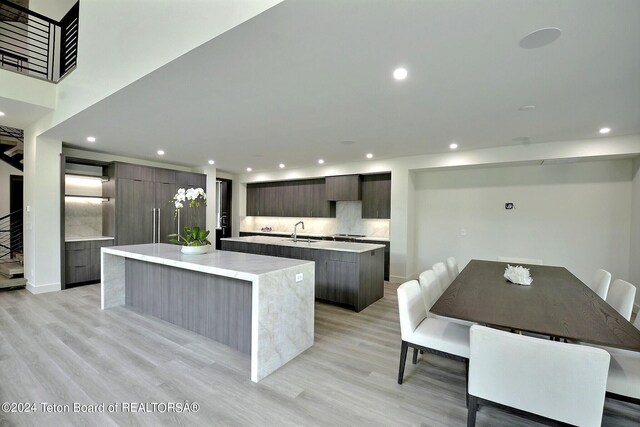 kitchen with a kitchen island, sink, backsplash, light hardwood / wood-style flooring, and dark brown cabinets