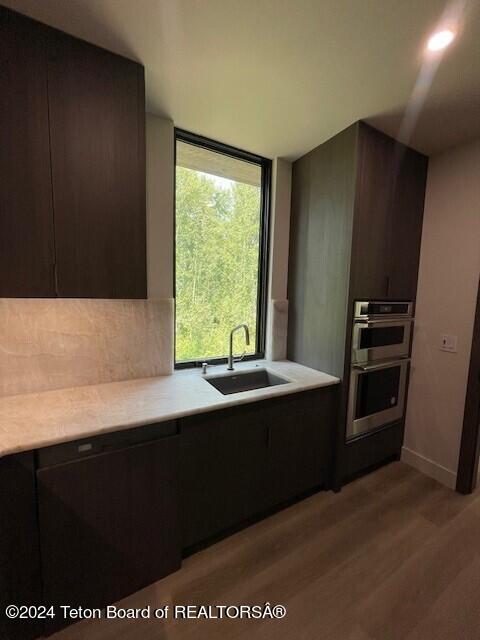 kitchen featuring floor to ceiling windows, sink, light hardwood / wood-style flooring, stainless steel double oven, and dark brown cabinets