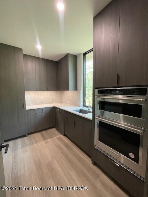 kitchen featuring stainless steel double oven, dark brown cabinets, sink, and light hardwood / wood-style floors