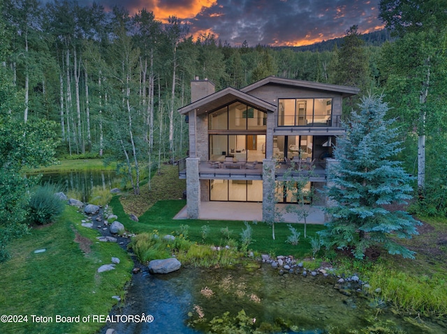 back house at dusk featuring a patio area, a lawn, and a balcony