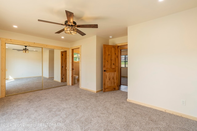 unfurnished bedroom featuring a closet, ensuite bathroom, carpet floors, and ceiling fan