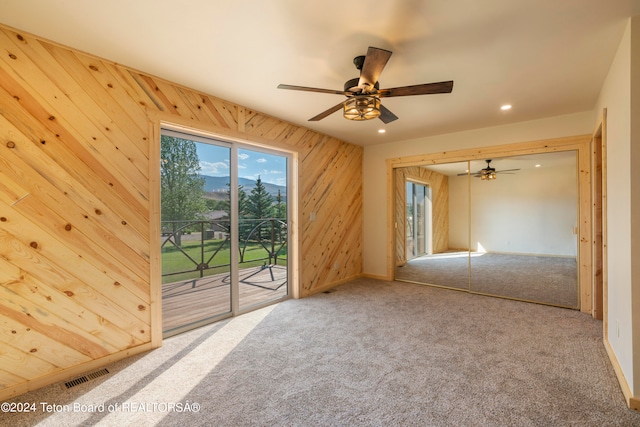 empty room with carpet floors, wooden walls, and ceiling fan