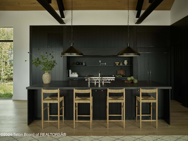 kitchen with a breakfast bar area, light wood-type flooring, beamed ceiling, pendant lighting, and sink