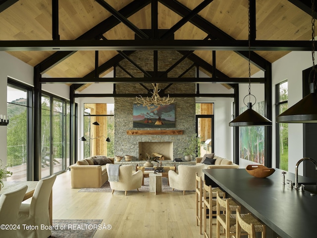 dining area with wooden ceiling, high vaulted ceiling, beamed ceiling, light hardwood / wood-style floors, and a stone fireplace