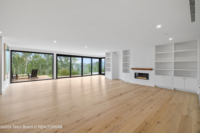 unfurnished living room featuring a wall of windows, built in features, and light wood-type flooring