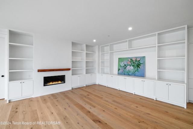 unfurnished living room featuring built in features and light wood-type flooring