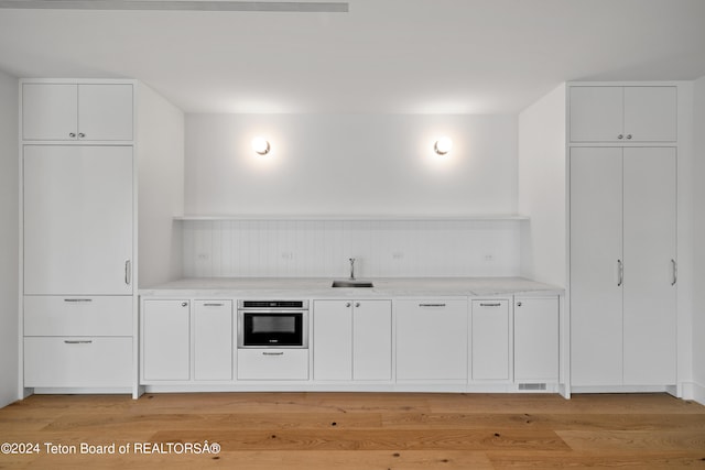 bar featuring sink, stainless steel oven, white cabinets, and light hardwood / wood-style floors