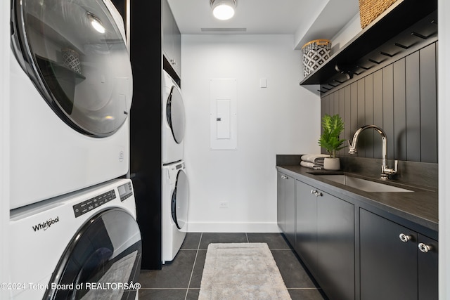 laundry area featuring stacked washer / drying machine, sink, dark tile patterned flooring, cabinets, and electric panel