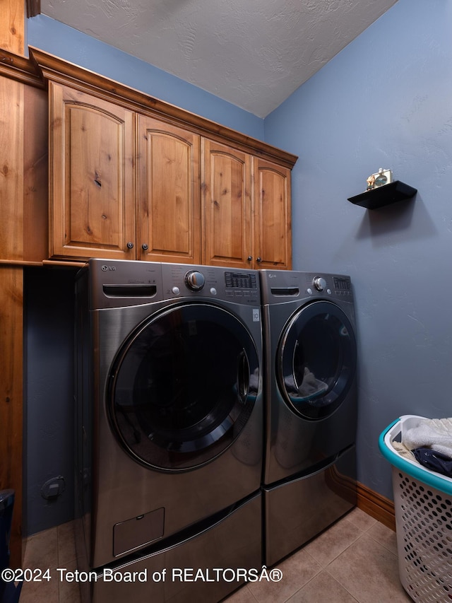 clothes washing area with cabinets, light tile patterned floors, washing machine and clothes dryer, and a textured ceiling