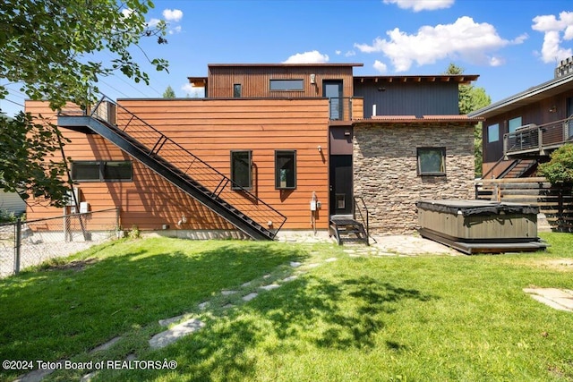 rear view of property with a hot tub and a yard