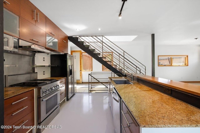 kitchen with appliances with stainless steel finishes, sink, light stone counters, and a center island