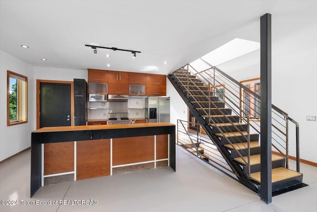 kitchen featuring exhaust hood, a skylight, stainless steel appliances, rail lighting, and a breakfast bar area