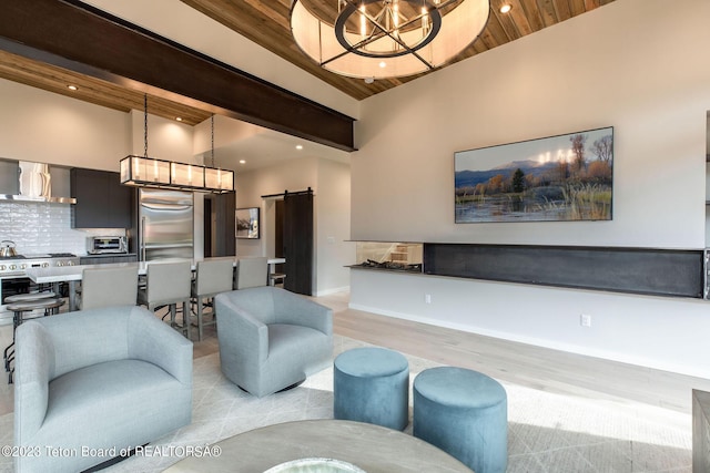 living room featuring a towering ceiling, a barn door, light hardwood / wood-style flooring, and wood ceiling