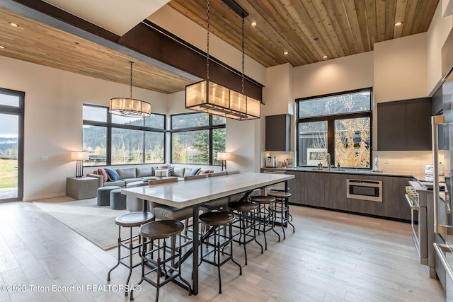 dining area featuring wood ceiling, light hardwood / wood-style floors, a towering ceiling, sink, and an inviting chandelier