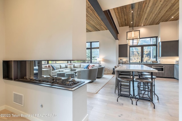 kitchen featuring a center island, light hardwood / wood-style floors, wood ceiling, a towering ceiling, and a kitchen breakfast bar