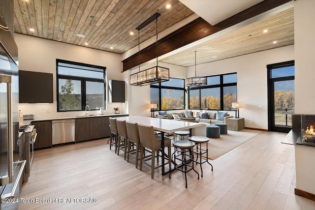 kitchen with stainless steel dishwasher, hanging light fixtures, a towering ceiling, light wood-type flooring, and backsplash