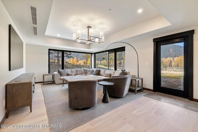 living room with an inviting chandelier, a tray ceiling, and light hardwood / wood-style flooring