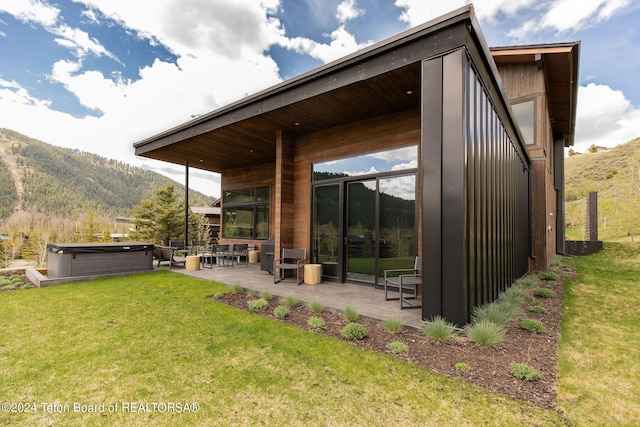 rear view of property featuring a hot tub, a mountain view, a patio area, and a lawn