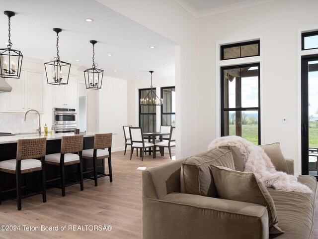 living room with sink, light hardwood / wood-style flooring, ornamental molding, and a notable chandelier