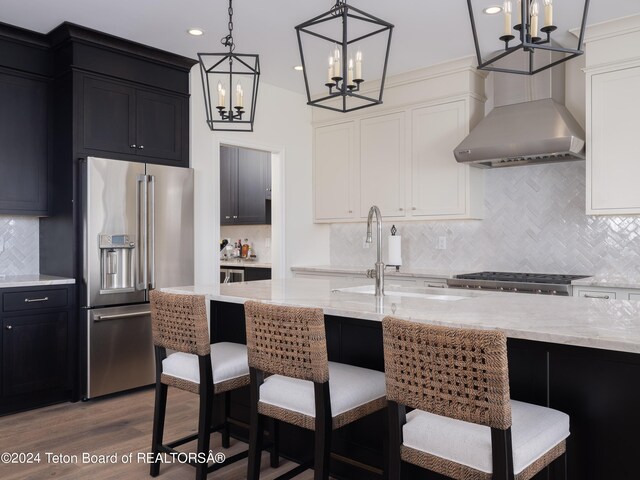 kitchen with decorative light fixtures, hardwood / wood-style flooring, white cabinets, wall chimney range hood, and high quality fridge