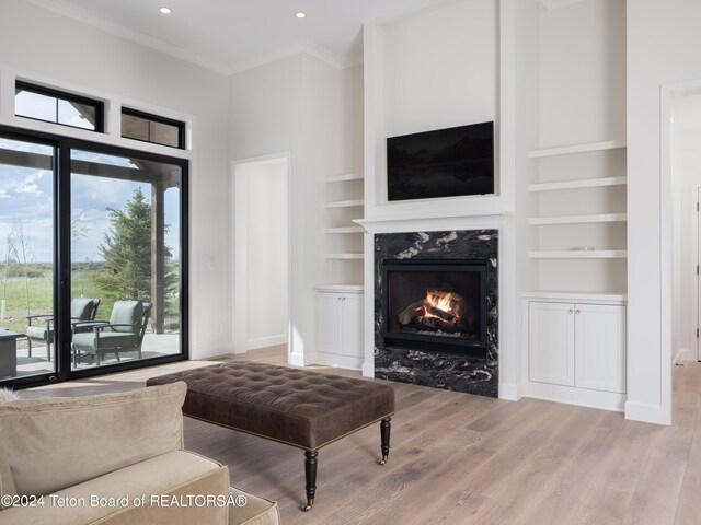 living room with hardwood / wood-style floors, built in shelves, crown molding, and a fireplace