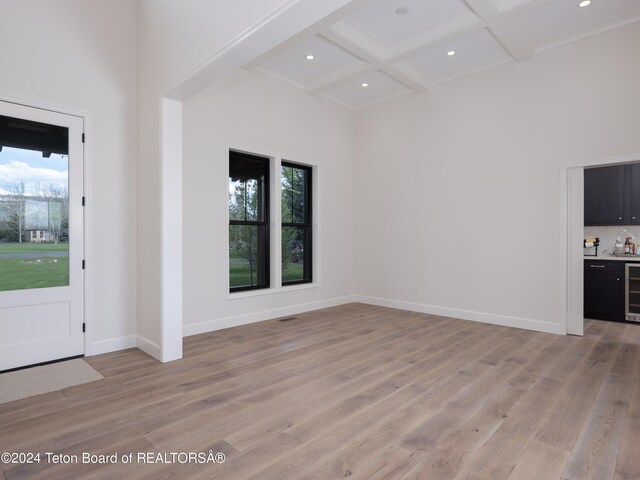 entrance foyer featuring beverage cooler, a towering ceiling, light hardwood / wood-style floors, beam ceiling, and coffered ceiling