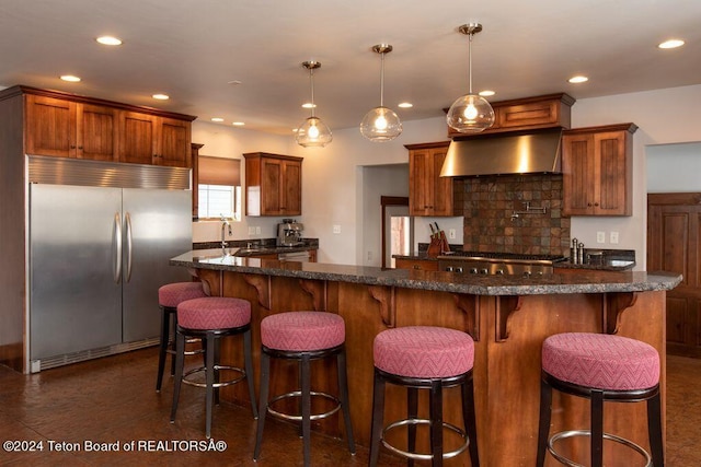 kitchen featuring recessed lighting, stainless steel appliances, wall chimney range hood, brown cabinets, and tasteful backsplash