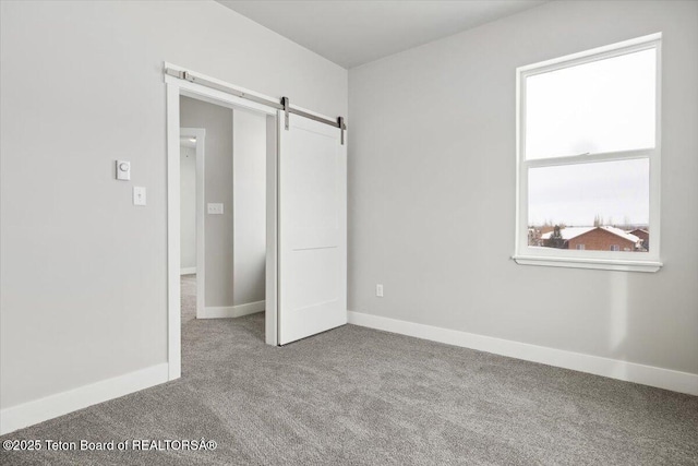 unfurnished bedroom featuring a barn door and carpet flooring