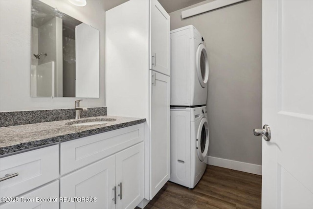 laundry area with sink, dark wood-type flooring, cabinets, and stacked washer / drying machine