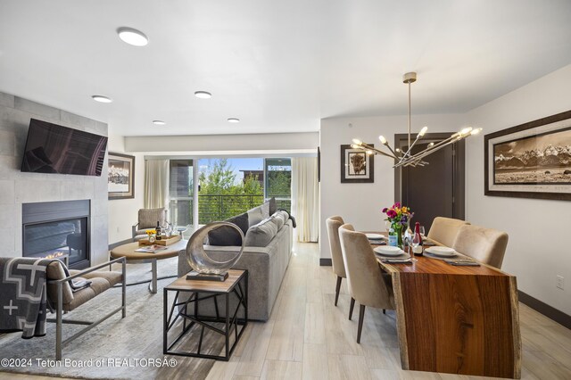 dining area with light hardwood / wood-style floors, an inviting chandelier, and a tiled fireplace