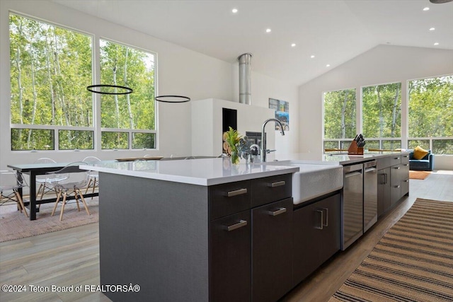 kitchen featuring light hardwood / wood-style flooring, stainless steel dishwasher, an island with sink, vaulted ceiling, and sink