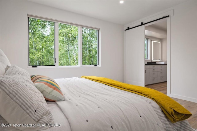 bedroom with ensuite bathroom, hardwood / wood-style flooring, and a barn door