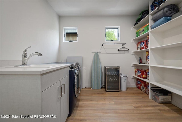 laundry area featuring washing machine and dryer, beverage cooler, light hardwood / wood-style flooring, and cabinets