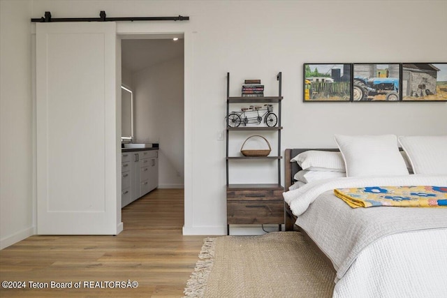 bedroom featuring light hardwood / wood-style floors, a barn door, and connected bathroom