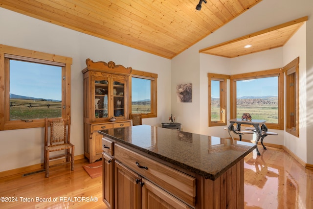 kitchen with lofted ceiling, dark stone countertops, a center island, wood ceiling, and light hardwood / wood-style floors